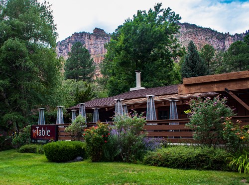 A rustic restaurant surrounded by greenery, with mountains in the background and outdoor seating under heaters.