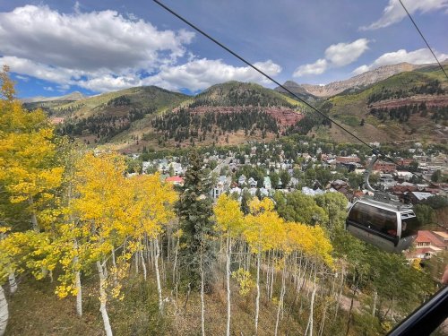 A scenic view from a gondola, showcasing a colorful mountain landscape and a town surrounded by autumn foliage.
