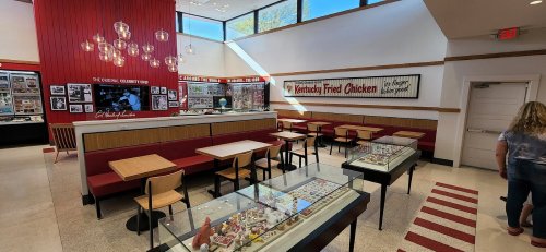 Interior of a restaurant featuring tables, display cases, and a red accent wall with KFC memorabilia.