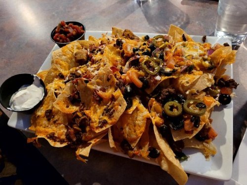A large plate of nachos topped with cheese, meat, jalapeños, and olives, served with salsa and sour cream on the side.