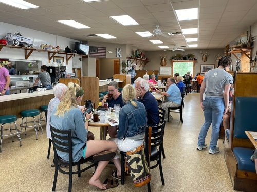 A busy diner with patrons seated at tables, enjoying meals and chatting in a cozy, rustic atmosphere.