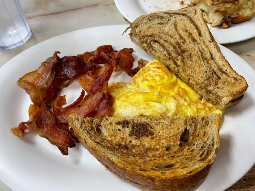 A plate with crispy bacon and a toasted sandwich filled with a fluffy omelet.