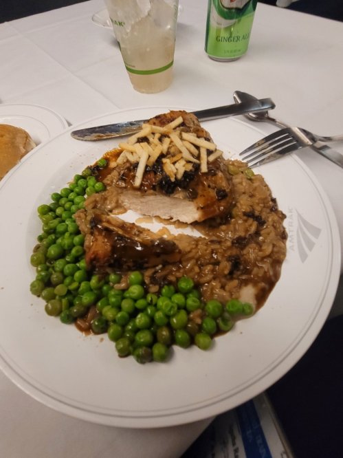 A plate of chicken with gravy, rice, and green peas, garnished with sliced apples, on a white tablecloth.