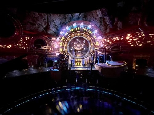 A futuristic, illuminated control room with a large circular display and intricate designs, set in a rocky environment.