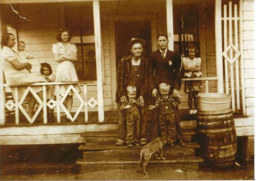 A sepia-toned photo of a family on a porch, featuring adults, children, and a dog, with a barrel nearby.