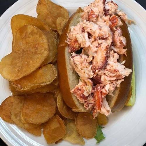 A lobster roll filled with lobster meat on a bun, served with a side of crispy potato chips.
