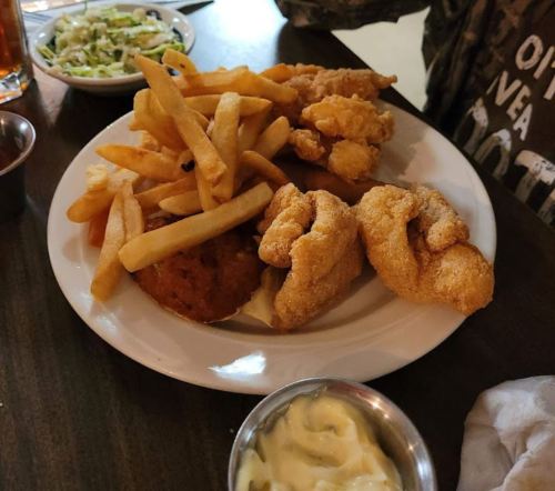 A plate of fried fish, chicken tenders, French fries, and a side of coleslaw with a small bowl of dipping sauce.