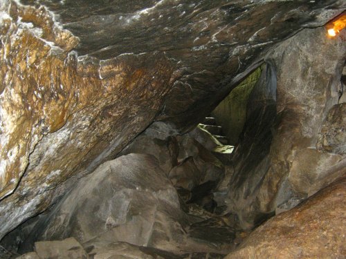 A dimly lit cave interior with rough stone walls and a narrow passage leading deeper into the darkness.