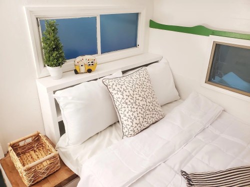 Cozy bedroom with a white bed, decorative pillow, small plant, and a toy bus on a windowsill.