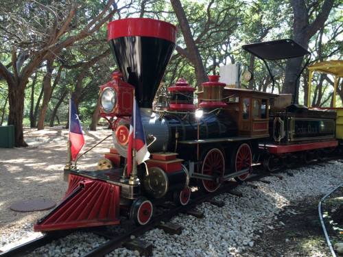 A vintage steam locomotive with red and black details, parked on a track surrounded by trees.