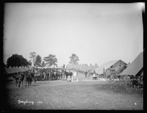 Black and white photo of a military camp at Gettysburg in 1910, featuring tents, soldiers, and horses.