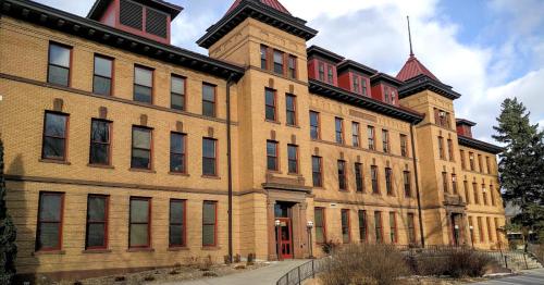 Historic brick building with red accents and a peaked roof, surrounded by trees and a cloudy sky.