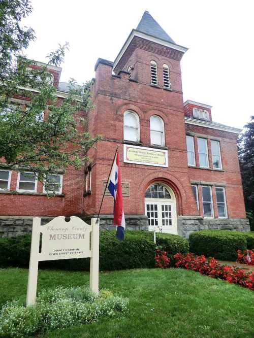 Historic brick building with a sign reading "Crawford County Museum" and a flag in front, surrounded by greenery and flowers.