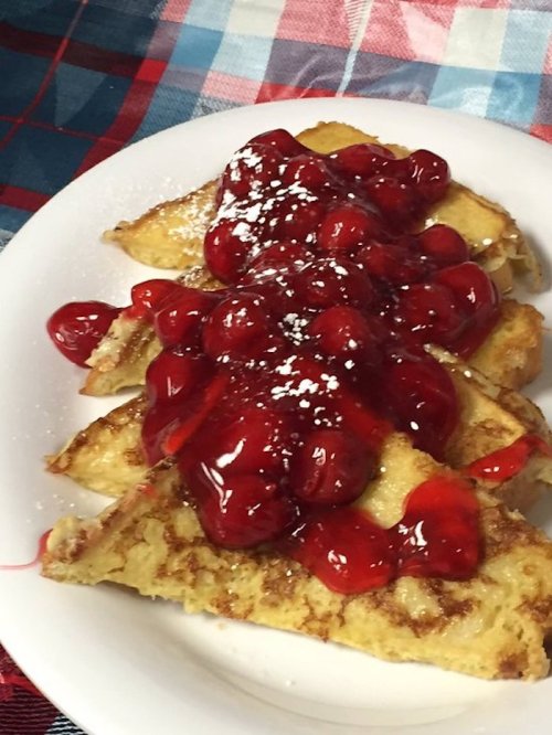 Three slices of French toast topped with cherry sauce and powdered sugar, served on a white plate.