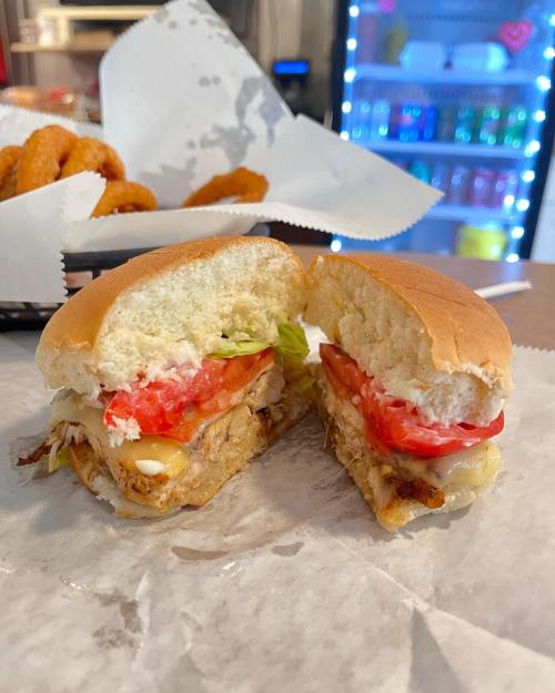 A freshly cut sandwich with grilled chicken, lettuce, tomato, and mayonnaise, served on a soft bun.