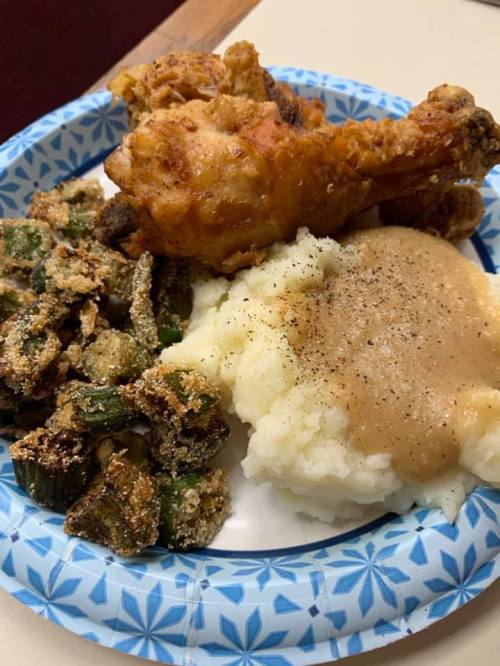 A plate of fried chicken, mashed potatoes with gravy, and fried okra on a paper plate.