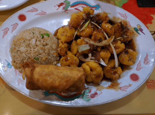 A plate of sweet and sour shrimp with fried rice and a spring roll, decorated with colorful patterns.
