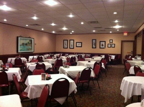 A spacious restaurant interior with neatly arranged tables, red chairs, and framed artwork on the walls.