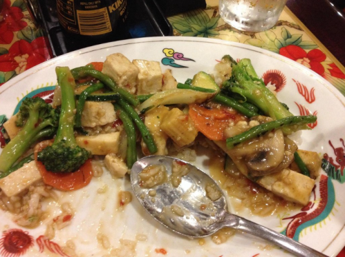 A plate of stir-fried vegetables with tofu, including broccoli, carrots, and mushrooms, served with rice.