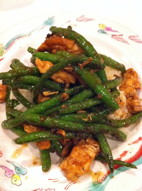 A plate of stir-fried chicken with green beans served over rice, garnished with herbs and spices.