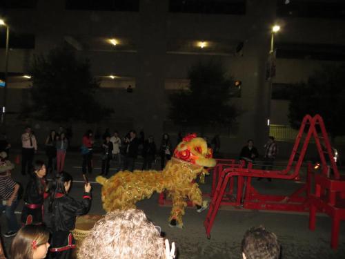 A lion dance performance takes place on a street, with spectators watching and a colorful lion costume in motion.