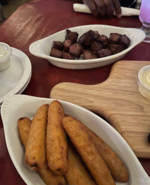 A plate of golden fried snacks and a dish of cubed, grilled meat on a red tablecloth.