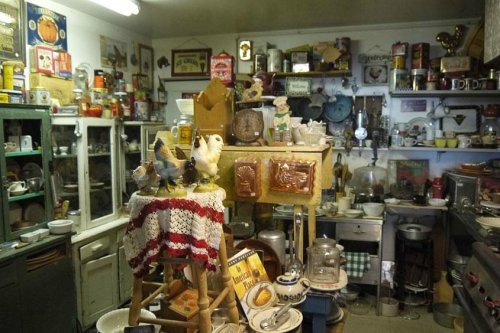 A vintage kitchen filled with various antiques, including dishes, decorations, and a wooden stool with figurines.