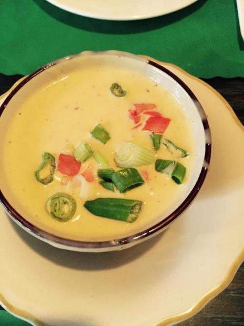A bowl of creamy soup with chopped green onions and diced tomatoes, served on a plate.