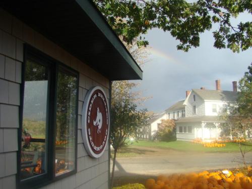 A farm scene featuring a building with a logo, pumpkins in the foreground, and a rainbow in the background.