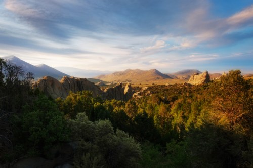 A scenic landscape featuring rocky formations, lush greenery, and distant mountains under a blue sky with wispy clouds.