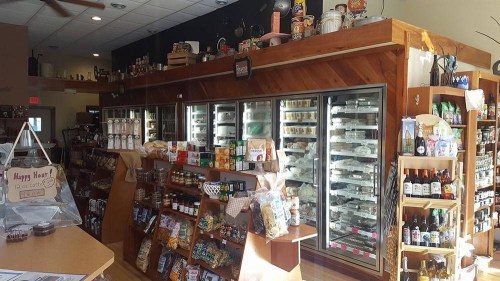 A cozy store interior featuring shelves of snacks, drinks, and a refrigerated display case. Warm lighting enhances the atmosphere.