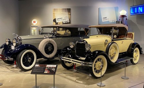 Two vintage cars on display: a gray 1929 Lincoln and a yellow 1927 Ford, showcasing classic automotive design.