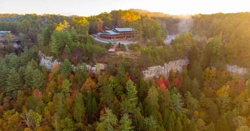 Aerial view of a lodge surrounded by colorful autumn trees and rocky cliffs in a scenic landscape.