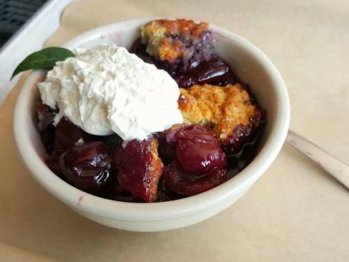 A bowl of cherry cobbler topped with whipped cream and a green leaf garnish.