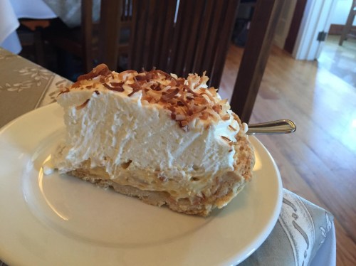 A slice of coconut cream pie topped with toasted coconut flakes on a white plate.