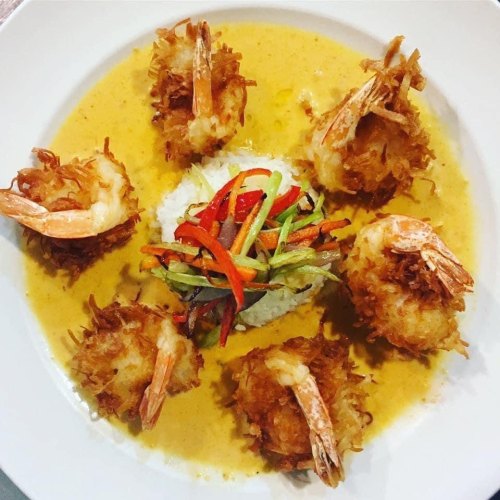 A plate of crispy coconut shrimp arranged around a mound of rice, topped with colorful julienned vegetables.