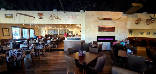 Interior of a rustic restaurant featuring wooden decor, a fireplace, and a menu board, with diners at tables.