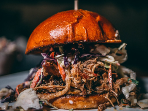 A close-up of a pulled pork sandwich topped with coleslaw on a toasted bun, served on a plate.