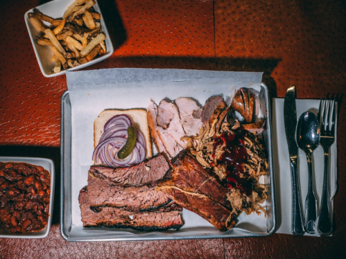 A tray with sliced meats, pickles, onions, and a side of baked beans and fries.