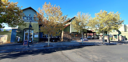 A restaurant with a green exterior and outdoor seating, surrounded by trees and a clear blue sky.