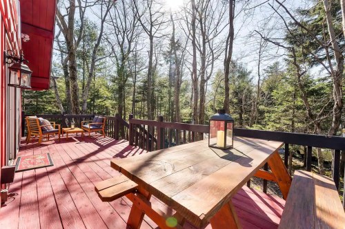A wooden deck with a picnic table and lantern, surrounded by trees and sunlight filtering through the branches.