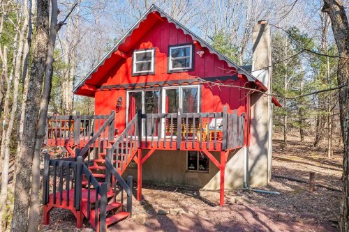 A charming red cabin with a deck, surrounded by trees in a serene outdoor setting.