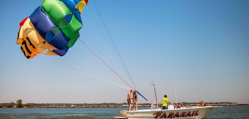 A colorful parachute is being launched from a boat with people enjoying parasailing on a sunny day.