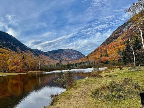 Scenic view of a tranquil river surrounded by colorful autumn foliage and mountains under a blue sky.