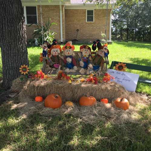 A festive display with scarecrows, pumpkins, and autumn decorations on a hay bale in a grassy area.
