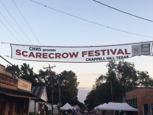 Banner for the Scarecrow Festival in Chappell Hill, Texas, hanging over a street with trees and buildings in the background.