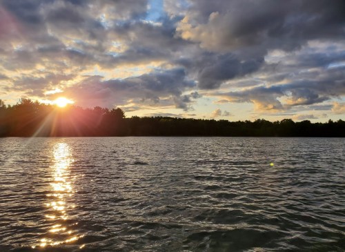 A serene lake at sunset, with golden light reflecting on the water and clouds scattered across the sky.