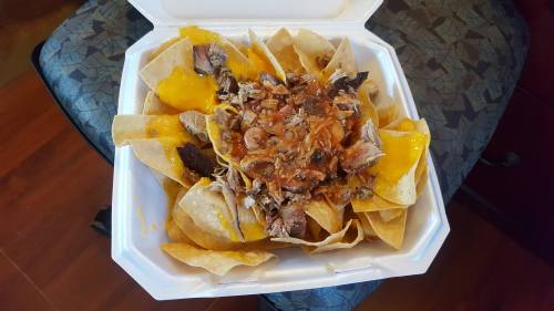 A takeout container filled with nachos topped with melted cheese, shredded meat, and a hearty bean mixture.