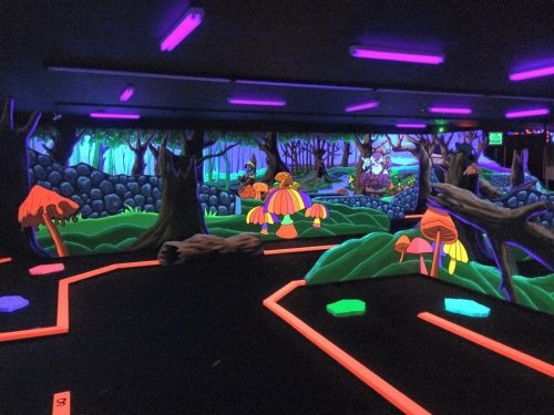 A vibrant, neon-lit mini-golf course featuring colorful mushrooms and a whimsical forest backdrop.