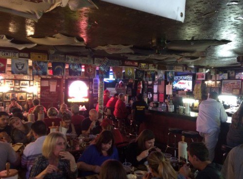 A lively bar scene with patrons dining, watching TV, and surrounded by sports memorabilia and colorful decor.